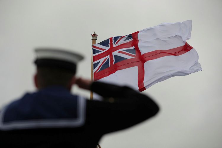 White Ensign being hoisted as a sailor salutes onboard HMS Prince of Wales for the first time during her commissioning FX190205033 CREDIT Crown Copyright